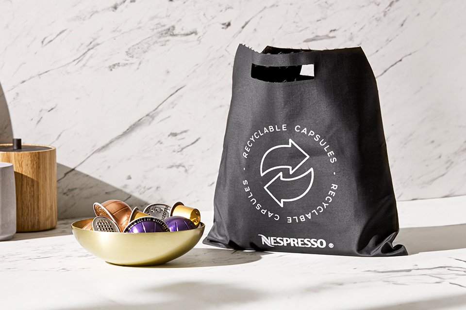 : A Nespresso recycling bag with multiple coffee capsules in a bowl beside it.